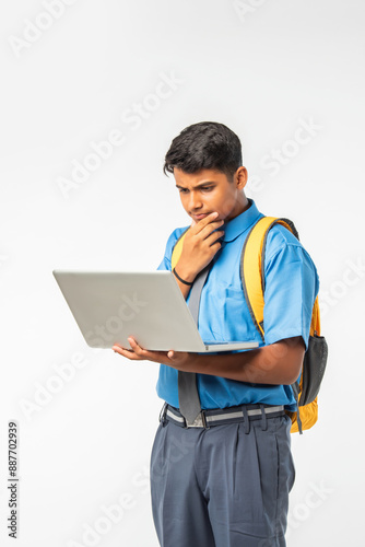 Indian Asian student in school uniform, holding laptop, isolated on white background, education concept © StockImageFactory