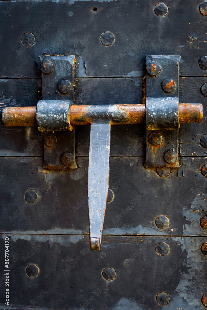 A close-up view of a rusty metal door bolt secured on a weathered black wooden door with antique features A close-up view of a rusty metal door bolt secured on a weathered black wooden door with antique features