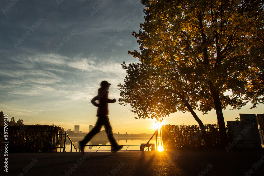 Woman running in a park at sunrise with beautiful autumn colors and lake in background