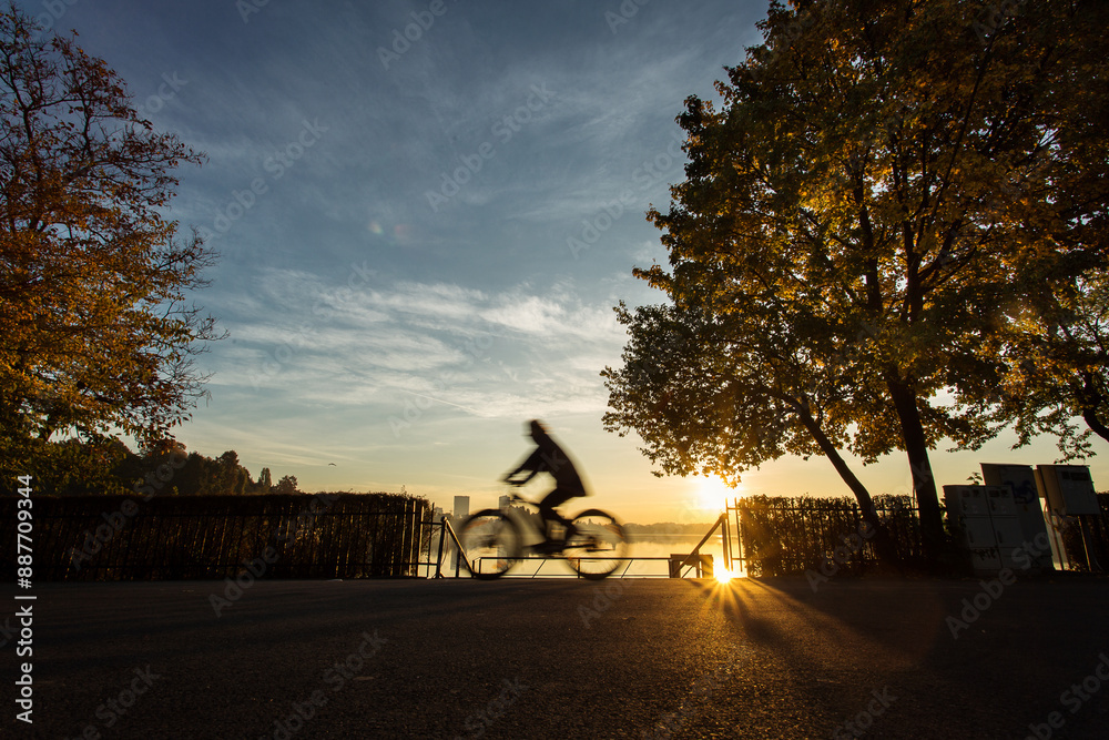 Man biking in a park at sunrise with beautiful autumn colors and lake in background