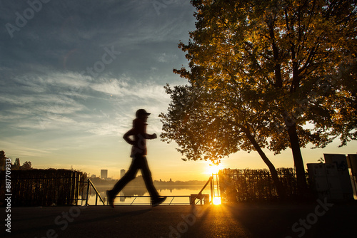 Obraz na płótnie Woman running in a park at sunrise with beautiful autumn colors and lake in background w salonie