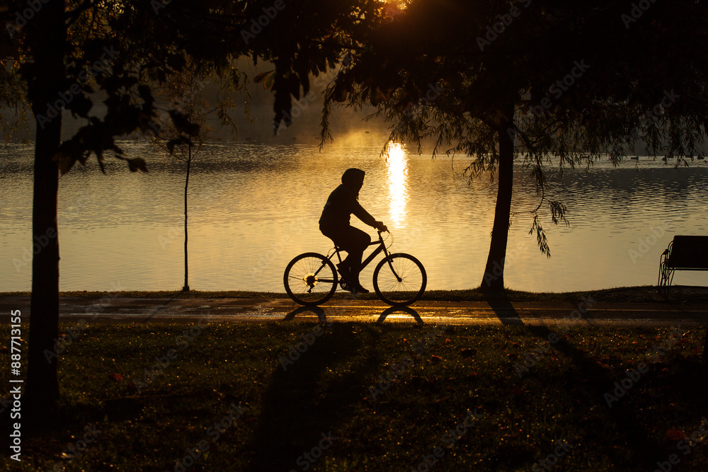 Man biking in a park at sunrise with beautiful autumn colors and lake in background