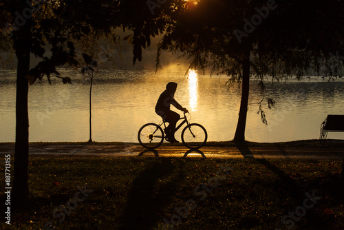 Obraz na płótnie Man biking in a park at sunrise with beautiful autumn colors and lake in background w salonie