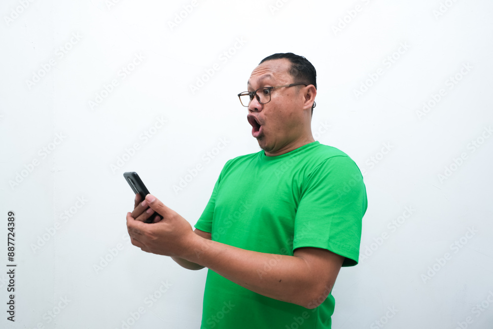 photo of the shocked expression of an Asian man looking at a mobile phone in his hand photo of the shocked expression of an Asian man looking at a mobile phone in his hand
