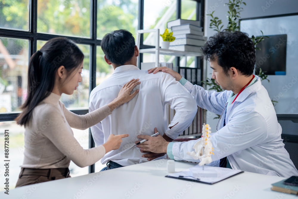 Fototapeta premium A doctor is examining a man's back while a woman looks on