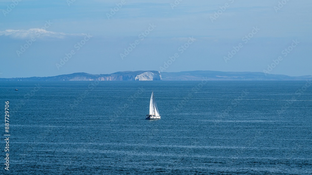 Fototapeta premium White sailboat at sea with the Isle of Wight in the background, Dorset Coast, Poole, England
