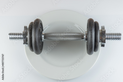 Gym dumbbell in the middle of a pottery plate, on white background. Concept useful for nutrition, fit, digestion, indigest.