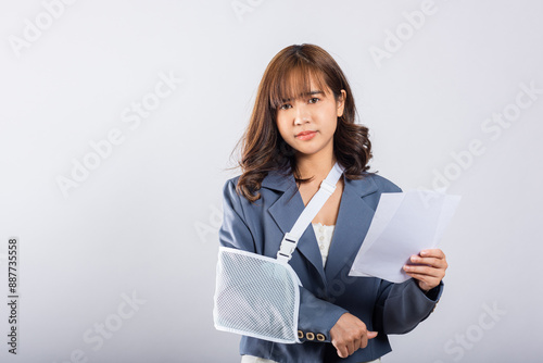 Depressed upset businesswoman arm in a splint after an accident, finds comfort in sling support from an excited while holding medical bills payment. Asian woman on white background, Broken arm