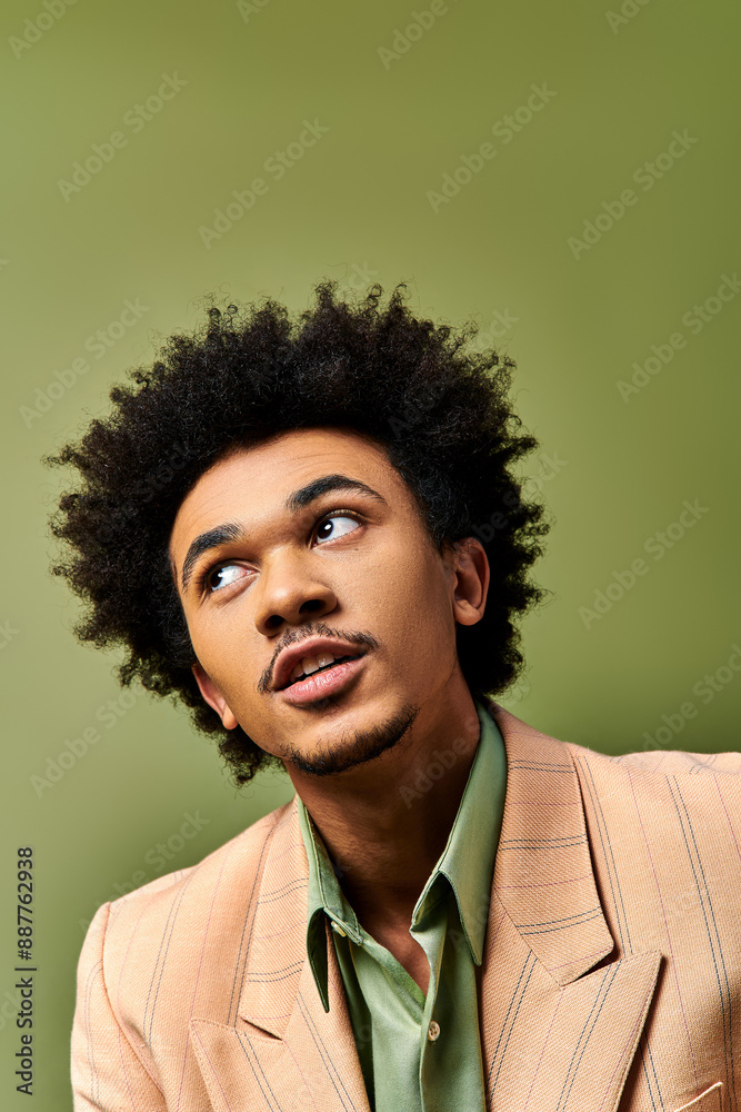Obraz premium A stylish young African American man with curly hair looks surprised against a green background.