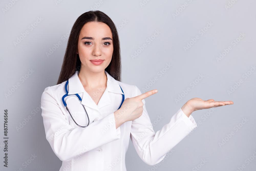Photo of professional medical worker lady indicate finger hold empty space white coat isolated on grey color background Photo of professional medical worker lady indicate finger hold empty space white coat isolated on grey color background