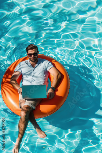 Young freelancer is using a laptop while floating on an inflatable ring in a swimming pool photo