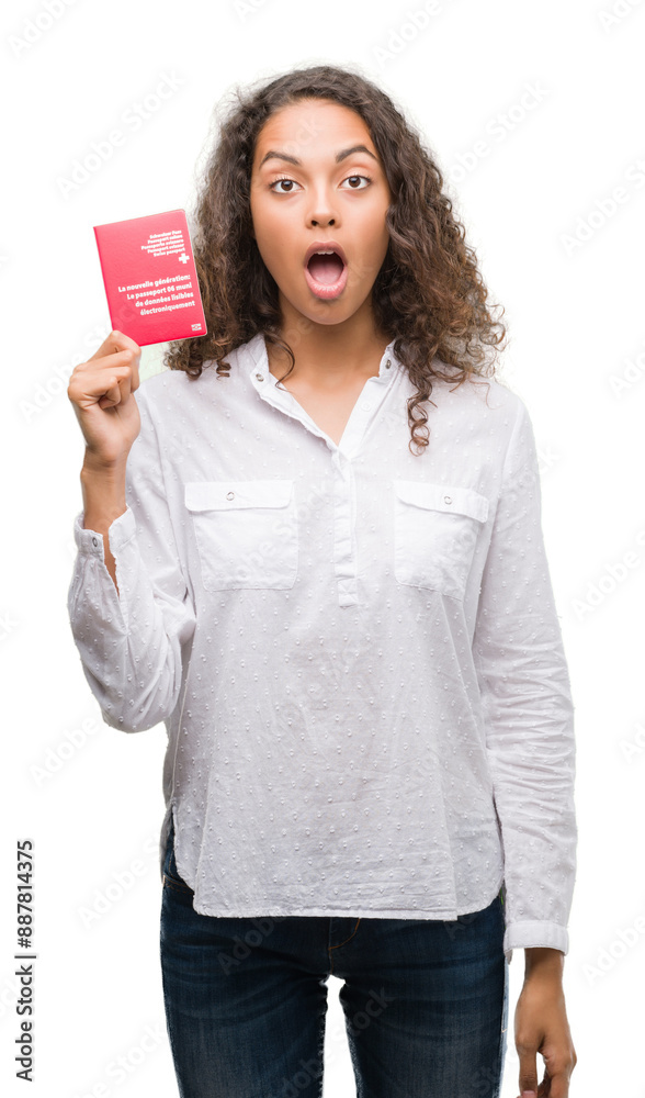 Young hispanic woman holding passport of Switzerland scared in shock with a surprise face, afraid and excited with fear expression