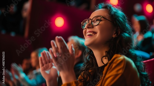 Joyful woman clapping with a smile, enjoying a theater show in a warmly lit auditorium.