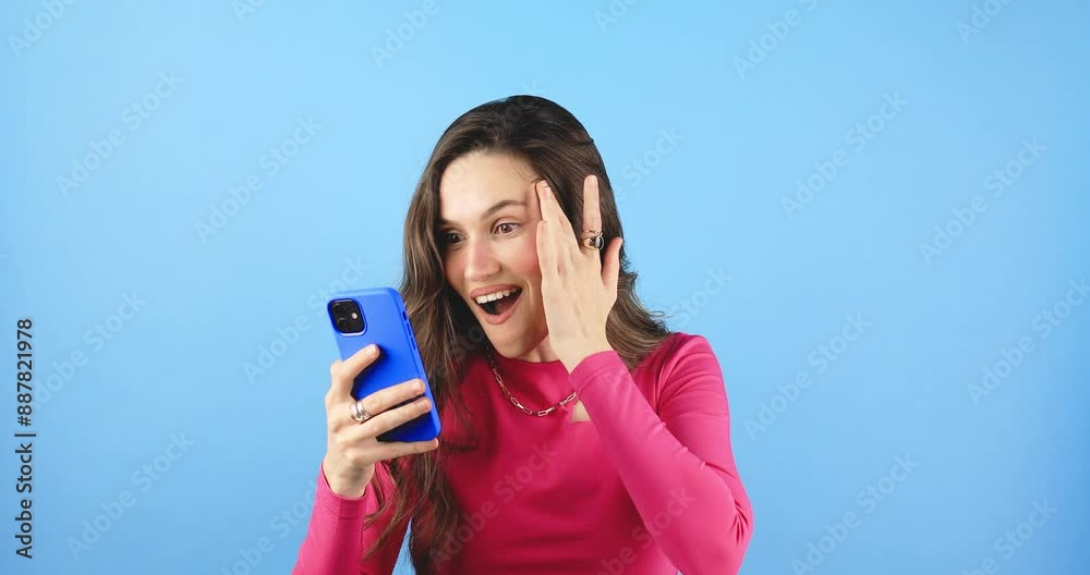 Attractive brunette woman look surprised wow hold using mobile cell phone on blue background. Girl look on smartphone and doing winner gesture. Girl just found out big win news, point on phone, wow. Attractive brunette woman look surprised wow hold using mobile cell phone on blue background. Girl look on smartphone and doing winner gesture. Girl just found out big win news, point on phone, wow.