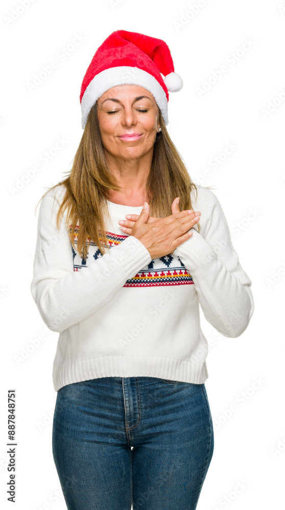 Middle age adult woman wearing winter sweater and chrismat hat over isolated background smiling with hands on chest with closed eyes and grateful gesture on face. Health concept. Middle age adult woman wearing winter sweater and chrismat hat over isolated background smiling with hands on chest with closed eyes and grateful gesture on face. Health concept.