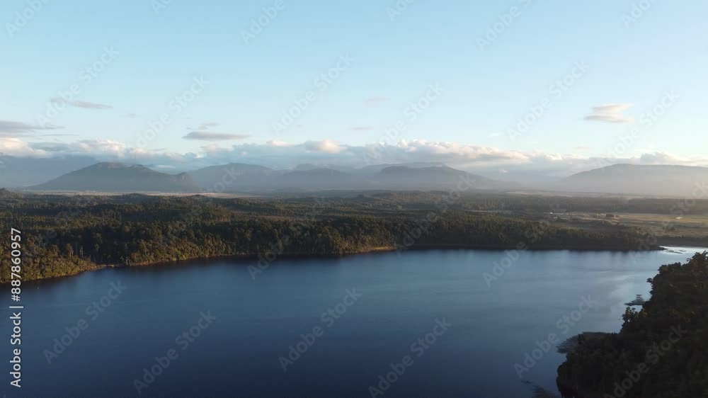 Drone view of lake Mahinapua in between forests and mountains during sunset at Hokitika, West Coast, New Zealand.
