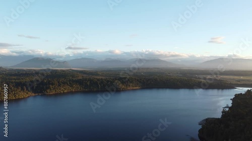 Drone view of lake Mahinapua in between forests and mountains during sunset at Hokitika, West Coast, New Zealand. photo