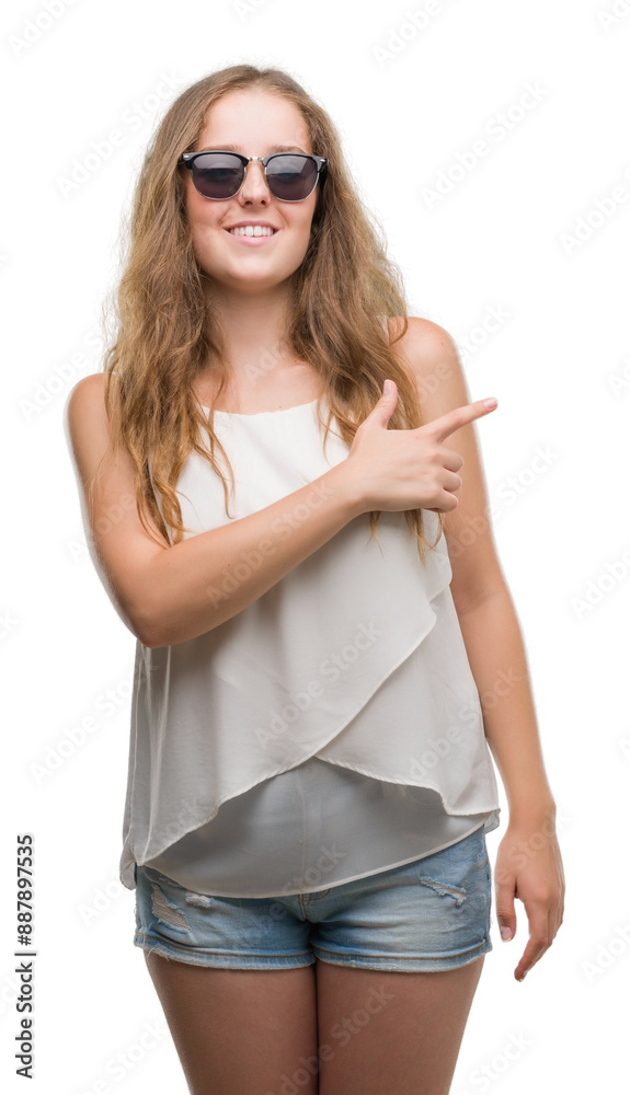 Young blonde woman wearing sunglasses cheerful with a smile of face pointing with hand and finger up to the side with happy and natural expression on face looking at the camera. Young blonde woman wearing sunglasses cheerful with a smile of face pointing with hand and finger up to the side with happy and natural expression on face looking at the camera.