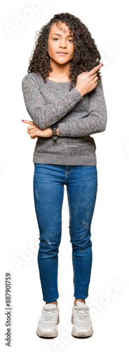 Young beautiful woman with curly hair wearing grey sweater Pointing with hand finger to the side showing advertisement, serious and calm face