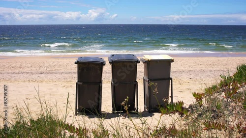 Three trash bins on a sandy beach with ocean waves in the background, waste management, beach cleanup, environmental protection