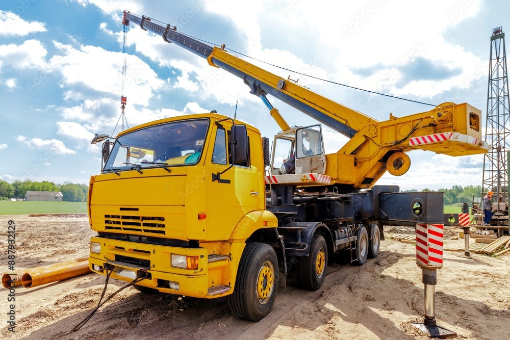 A large yellow truck crane stands ready to work on the construction site A large yellow truck crane stands ready to work on the construction site