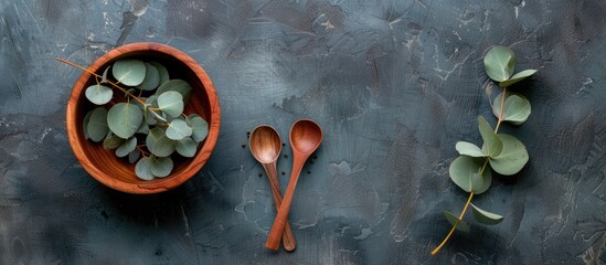 Top view of eucalyptus leaves next to a wooden bowl and spoon with copy space image