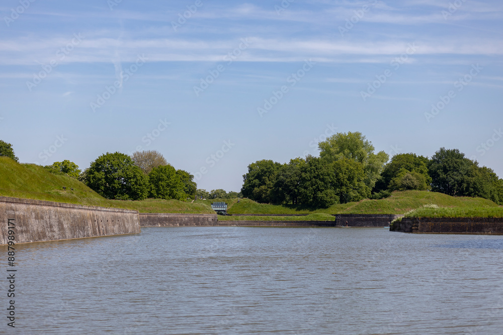 Greenery with church tower on top and behind Naarden Vesting moated Dutch stronghold city with defense structure bastion walls with canal in front Greenery with church tower on top and behind Naarden Vesting moated Dutch stronghold city with defense structure bastion walls with canal in front