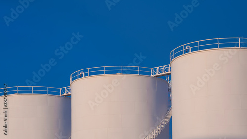 Row of 3 white storage fuel tanks against blue clear sky background, low angle view with copy space photo