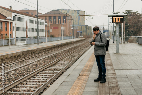 Man Checking Phone on Train Platform in City During Daytime