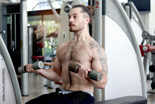 Strong young muscular man lifting dumbbell at gym. Handsome sport man doing weightlifting exercise at fitness. Athletic workout weight training, doing bodybuilding program for healthy and perfect body