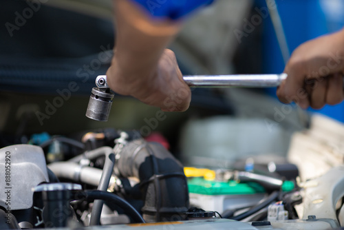 Auto mechanic repairs engine and uses wrench to tighten car screws.