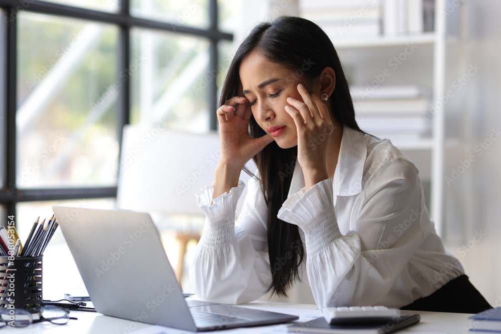 A woman in the office is stressed and has a headache from overwork. Tired business woman sleepy and bored from sitting at a desk for a long time and has office syndrome. A woman in the office is stressed and has a headache from overwork. Tired business woman sleepy and bored from sitting at a desk for a long time and has office syndrome.