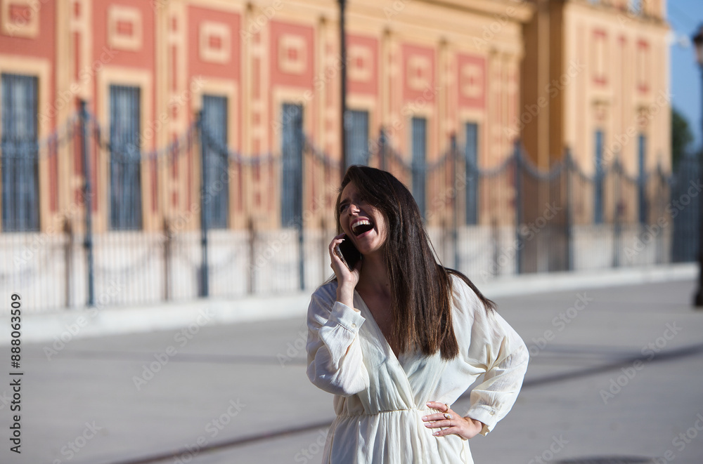 Young and beautiful Latin woman talking on mobile phone is having fun and is happy and smiling loudly. The woman is on the street and walks through the city. Concept communications. Young and beautiful Latin woman talking on mobile phone is having fun and is happy and smiling loudly. The woman is on the street and walks through the city. Concept communications.