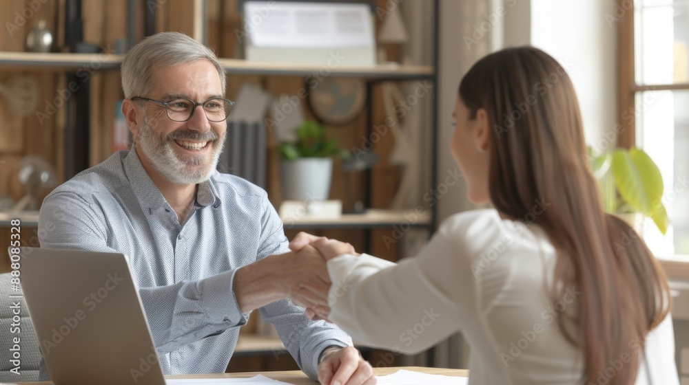Obraz premium Smiling middle-aged business man shaking hands with partner while making partnership collaboration agreement. Human resources manager and new hire shaking hands during onboarding interview.