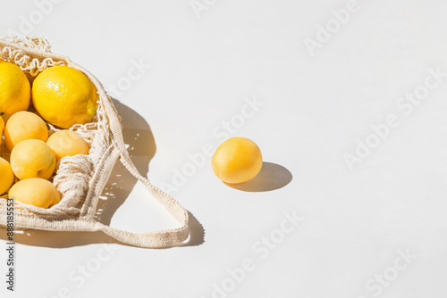 Fresh lemon and apricot fruits in a string bag on a white sunlit background. Healthy food concept. Eco friendly theme