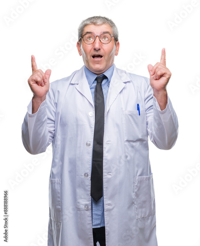 Handsome senior doctor, scientist professional man wearing white coat over isolated background amazed and surprised looking up and pointing with fingers and raised arms.