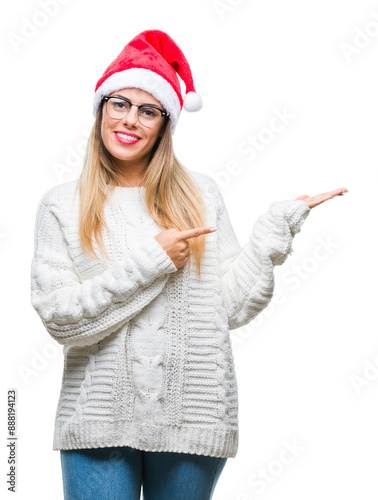 Young beautiful woman wearing christmas hat over isolated background amazed and smiling to the camera while presenting with hand and pointing with finger.