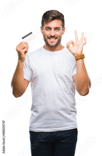 Young handsome man holding credit card over isolated background doing ok sign with fingers, excellent symbol