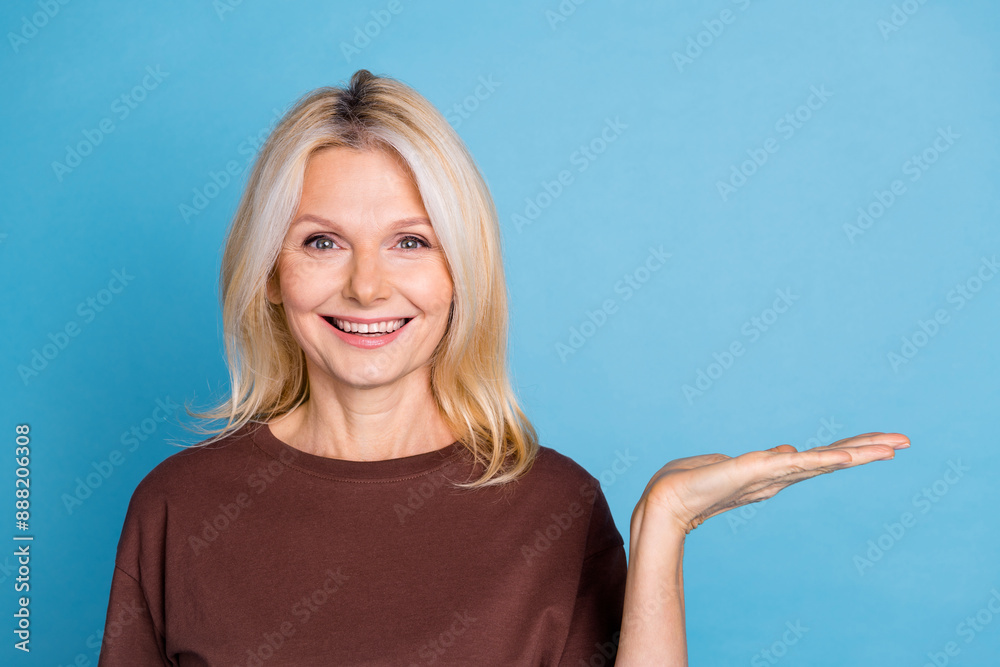 Fototapeta premium Photo of positive pretty lovely senior woman wear brown clothes introduce empty space isolated on blue color background