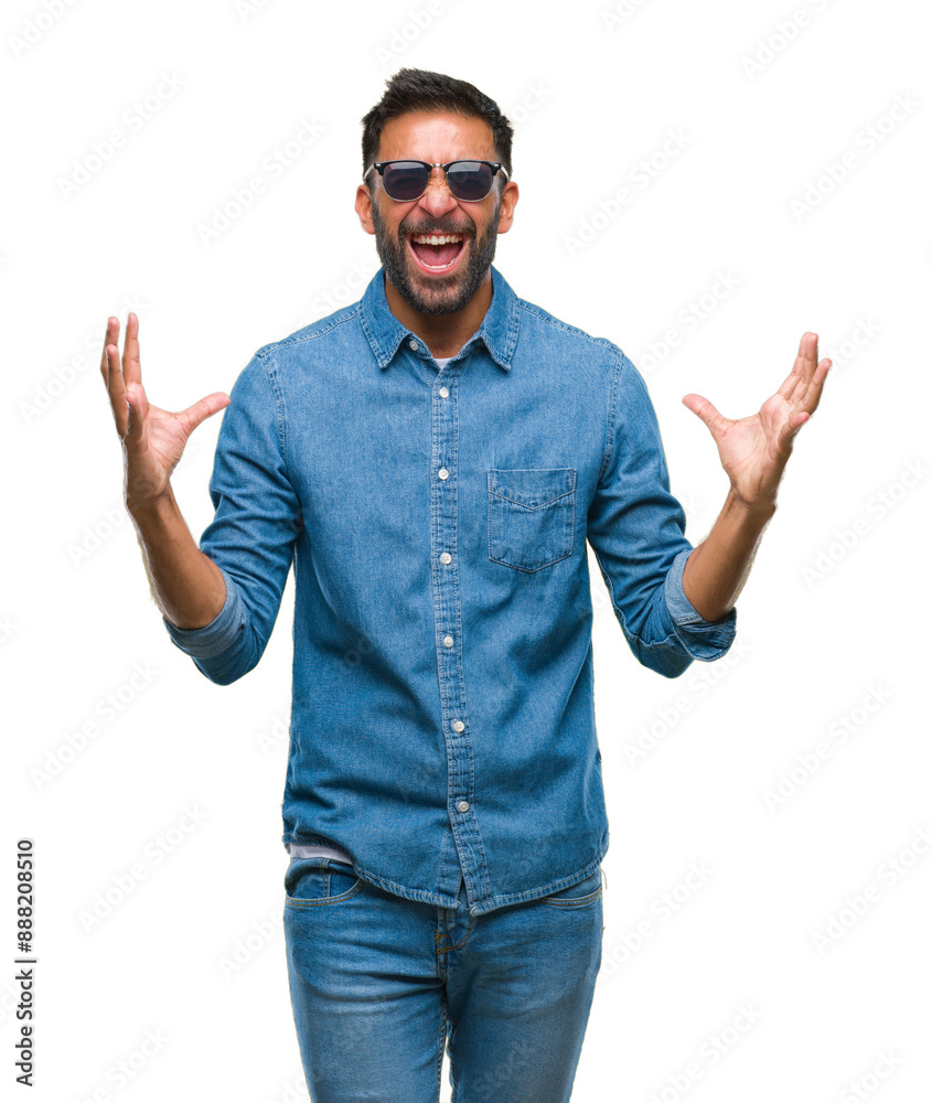 Adult hispanic man wearing sunglasses over isolated background crazy and mad shouting and yelling with aggressive expression and arms raised. Frustration concept.