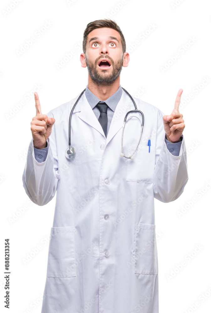 Young handsome doctor man over isolated background amazed and surprised looking up and pointing with fingers and raised arms. Young handsome doctor man over isolated background amazed and surprised looking up and pointing with fingers and raised arms.