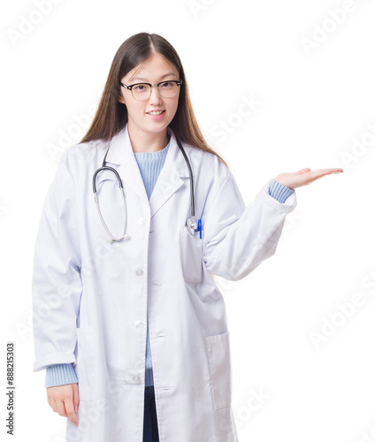 Young Chinese doctor woman over isolated background smiling cheerful presenting and pointing with palm of hand looking at the camera.