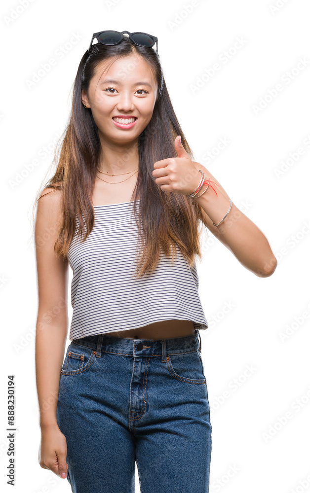 Young asian woman wearing sunglasses over isolated background doing happy thumbs up gesture with hand. Approving expression looking at the camera with showing success. Young asian woman wearing sunglasses over isolated background doing happy thumbs up gesture with hand. Approving expression looking at the camera with showing success.