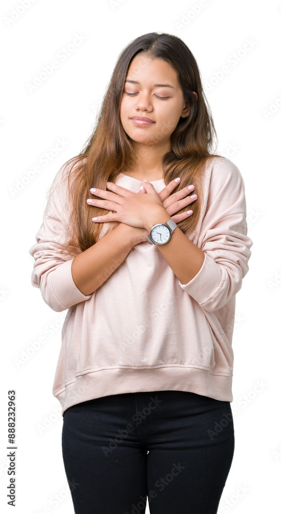 Young beautiful brunette woman wearing pink sweatshirt over isolated background smiling with hands on chest with closed eyes and grateful gesture on face. Health concept.