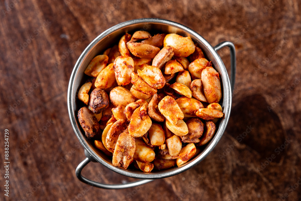 A metal cup filled with roasted nuts on a wooden surface