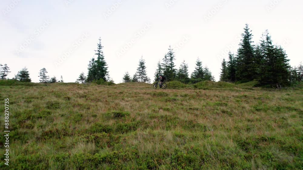 Cyclist man riding electric mountain bike outdoors. Male tourist biking along grassy trail in the mountains, wearing helmet and backpack. Concept of sport, active leisure and nature. Cyclist man riding electric mountain bike outdoors. Male tourist biking along grassy trail in the mountains, wearing helmet and backpack. Concept of sport, active leisure and nature.