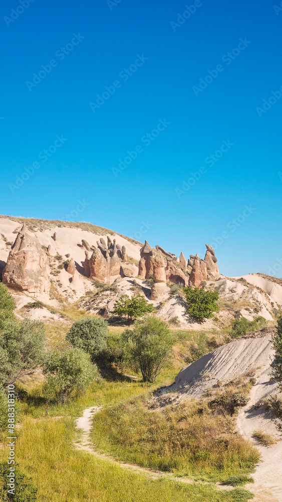 Fototapeta premium Landscape with path through imagination valley national geology park with fantastic volcanic tuff formations, green grass and bushes and clear blue sky is a travel destination for hiking or trekking