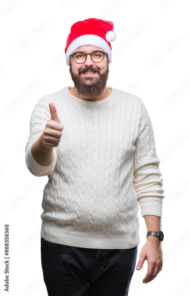 Young caucasian man wearing christmas hat and glasses over isolated background doing happy thumbs up gesture with hand. Approving expression looking at the camera with showing success. Young caucasian man wearing christmas hat and glasses over isolated background doing happy thumbs up gesture with hand. Approving expression looking at the camera with showing success.