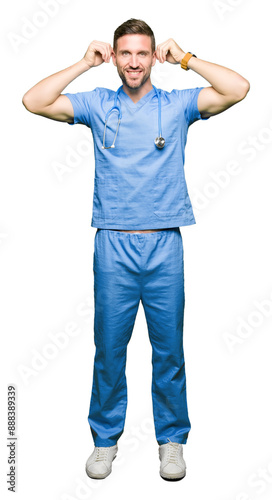 Handsome doctor man wearing medical uniform over isolated background Smiling pulling ears with fingers, funny gesture. Audition problem