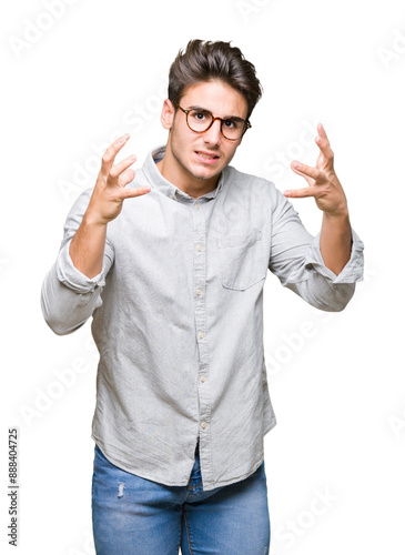 Young handsome man wearing glasses over isolated background Shouting frustrated with rage, hands trying to strangle, yelling mad